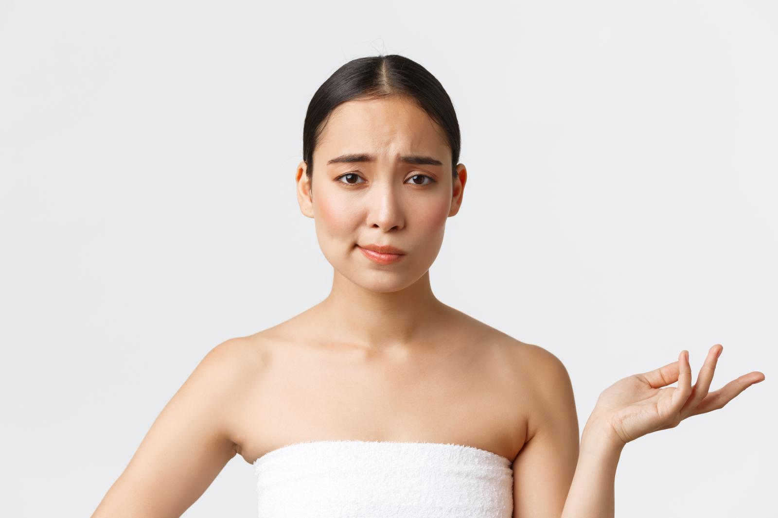 woman-wrapped-in-a-bath-towel-standing-against-a-white-background-raising-one-hand-in-a-careless-gesture-while-smirking